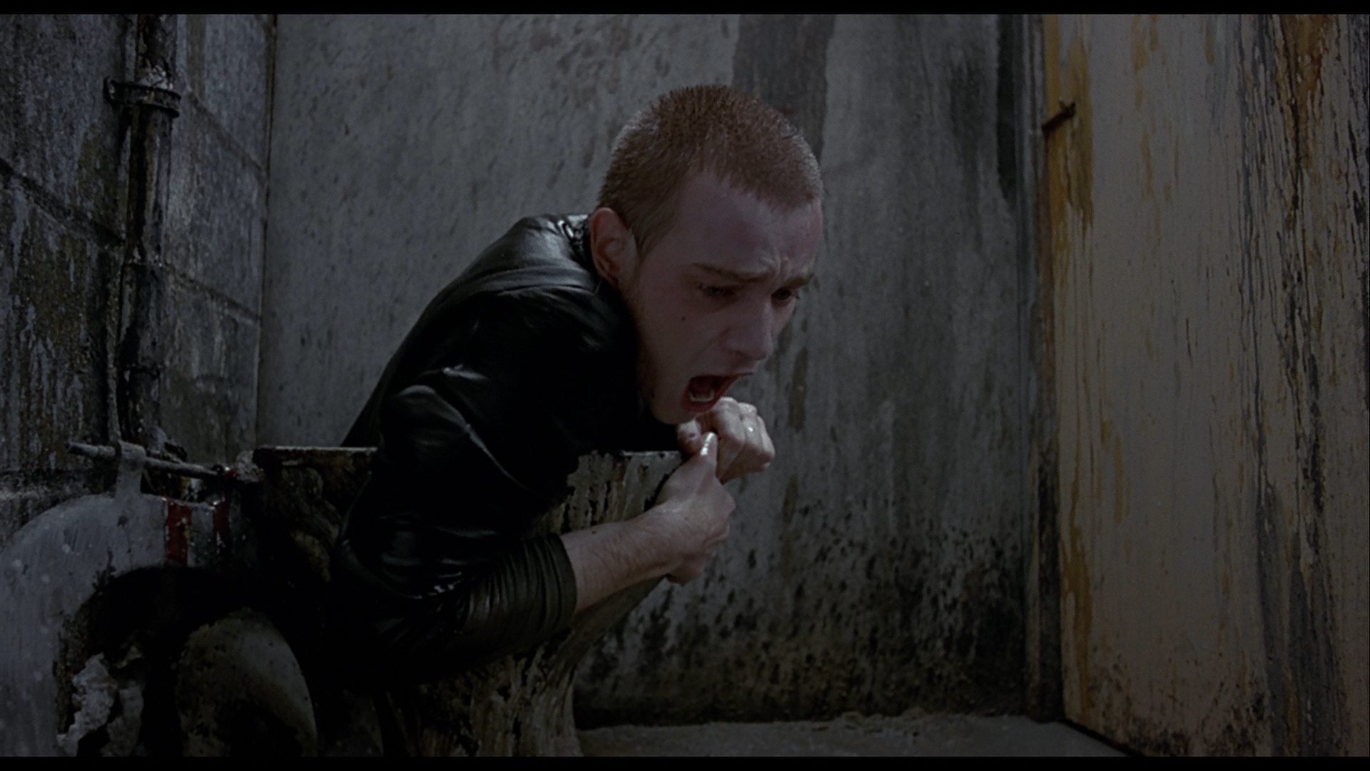 Rent (incarné par Ewan McGregor) sort d'une cuvette de toilettes crasseuse. Image issue du film Trainspotting réalisé par Danny Boyle.
